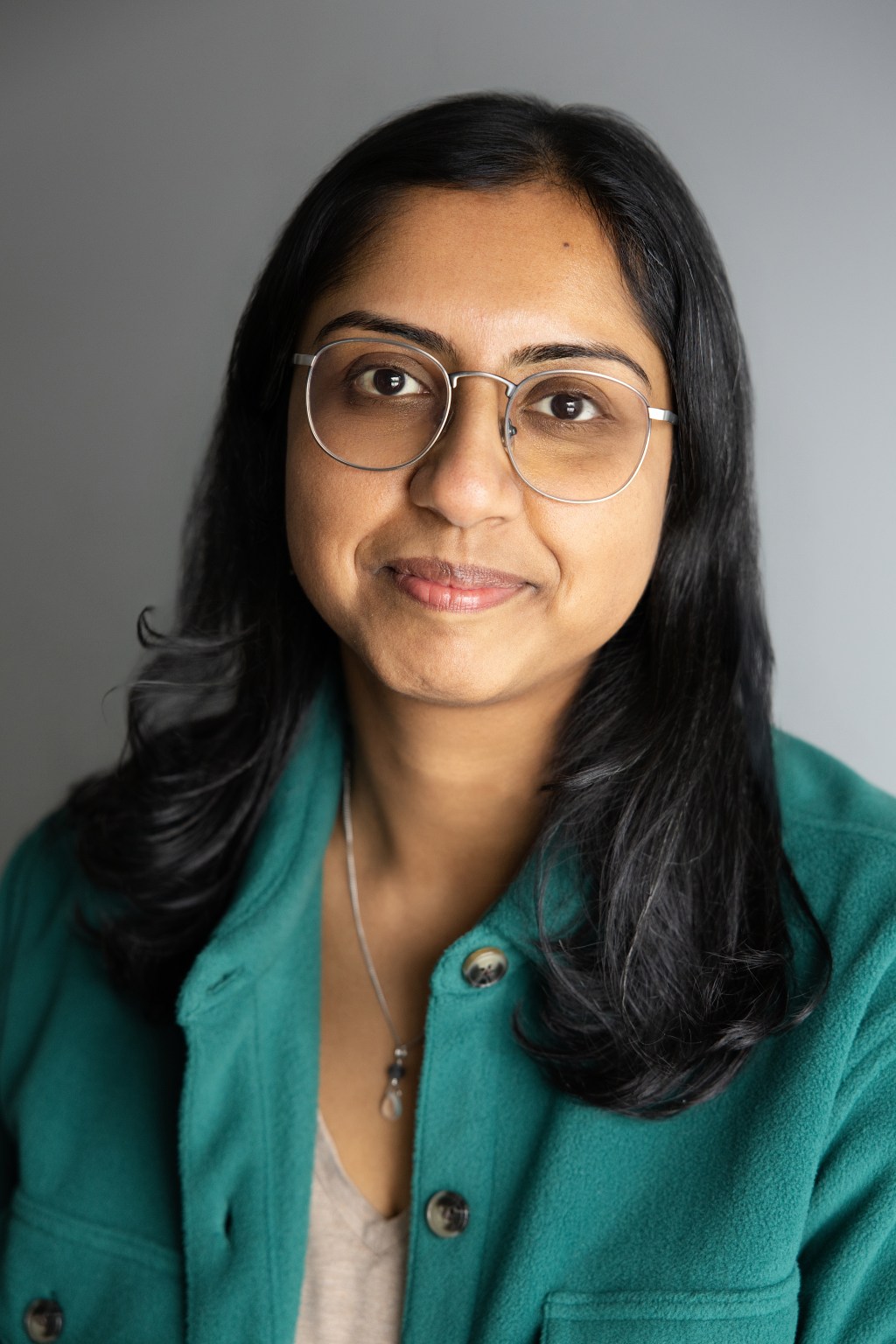 Woman with brown skin and black hair wearing a green shirt and glasses.